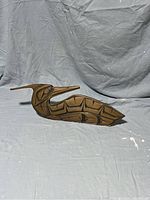 Front view of the hand-carved loon showing detailed Indigenous Kwakiutl formline design in dark paint over wood surface, elongated shape with long beak.