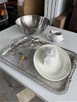 Photo of the whole lot showing a silver bowl, an ornate silver tray holding a butter dish, swan mug, and a silver-handled utensil on a white table.