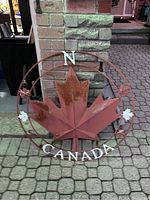 Front view of circular metal maple leaf decoration with rust and the text "CANADA" and letter "N".