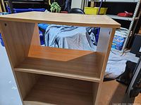 Front view of melamine shelf unit showing three levels and wood-colored finish with some damage on top surface
