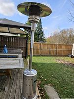 Full view of the propane patio heater standing on a backyard wooden deck with a wooden fence and garden furniture in the background