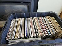 Large black plastic bin filled with numerous vinyl records, viewed from above.