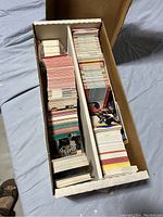 Wide shot of cardboard box filled with organized stacks of sports cards primarily hockey and basketball