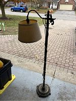 Full view of the standing lamp showing twisted metal pole, heavy decorative cast iron base, and beige lampshade.