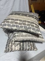 Three rectangular throw pillows stacked showing gray fabric with black abstract brick-like pattern