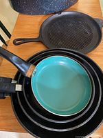 Photo showing stacked frypans including a cast iron grill pan and a turquoise-colored non-stick frypan.