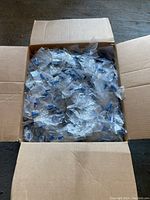 Open cardboard box filled with multiple clear plastic packs of screws and blue wall plugs.