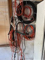 Wide view of all extension cords and garden hose coiled and hung on wall hooks in garage environment