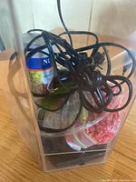 Side view of the clear rectangular fish tank with cords, fish food can, and plastic bag of pellets inside.