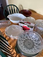 Pyrex mixing bowl, wooden bowl, glass loaf pan, Corningware dishes with lids, Crock-Pot box, two Pyrex measuring cups, and small glass bowl on wooden table