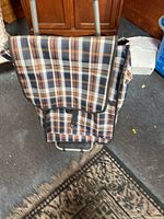Front angle of the grocery trolley showing the plaid fabric bag with flap and Velcro strap, metal frame, and part of the wheel.