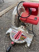 Tradesman M2500C mitre saw with red motor housing, silver base, clear blade guard, and black adjustment handle on outdoor ground surface.