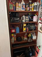 Front view of wooden shelving unit holding multiple shelves filled with automotive fluids, tools, and maintenance supplies.