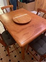 Photo showing the wooden dining table with scratches and wear, the round wooden lazy Susan on top, and four chairs surrounding it.