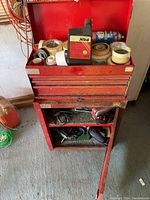Overall view of the red tool cabinet with tapes and oil bottle on top and power tools in lower compartment.