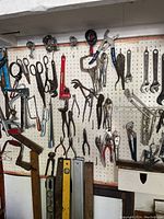 Wide view of pegboard wall holding numerous hand tools including pliers, scissors, wrenches, and small saws.