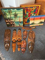 Top-down view of 5 wooden wall masks, 3 paintings, and bull horns arranged on floor.