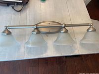 Front view of the 4-light brushed nickel wall sconce with frosted glass shades on white wood background, showing metal structure and glass shades.