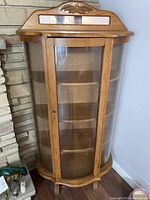 Front view of solid oak curved glass display cabinet with wooden shelves inside.