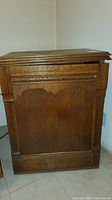 View of the front and side of the antique wooden sewing cabinet, showing carved detailing and general shape.