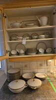 Full kitchen cabinet display of dishes including cups, saucers, pots, and plates.