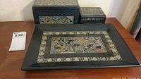 Set of two decorative boxes and one tray in black lacquer with intricate floral and bird motifs in gold and muted colors.