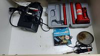 Motomaster 2 Ton hydraulic jack in carrying case next to black Eliminator intelligent battery charger with red and black alligator clips and other miscellaneous small items including a box of Thermog adhesive bandages.