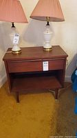 Front view of Kaufman Furniture wooden night stand with white lamps on top, showing drawer and open shelf
