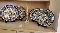 Overview of four hand painted ceramic plates and two candle holders on display