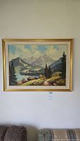 Full view of the framed painting showing the mountain landscape and lake scene hung on a wall above furniture.