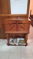 Front view of closed wooden sewing basket on stand with lower shelf and fabric bundles.