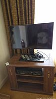 Samsung 32" TV showing full front view on wood entertainment stand with remotes and cables on top and Magnavox VCR/DVD player in bottom shelf