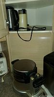 Waffle maker, coffee grinder, and kettle on kitchen shelves and counter