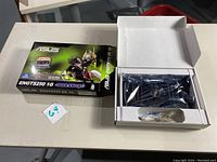 Asus ENGTS250 1G Dark Knight graphics card partially unpacked beside its box on table.