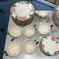 Photo showing stacked dinner plates, salad/soup bowls, and coffee cups with floral Desert Rose pattern around rims.