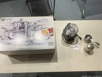 Top view of full lot on table: unopened JC Penney cookware box, Cuisinart food processor with cord, metal measuring cup set, and metal shaker container