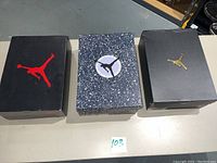 Three Jordan shoe boxes side by side (two black Jumpman logo boxes and one speckle-pattern box)