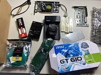 Lot overview showing MSI GT 610 graphics card box, Fenvi wireless adapter, sealed Cat 6 cable, silicon thermal grease, multiple circuit boards and RAM sticks.