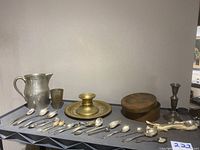 Wide view photo showing all items in the lot including spoons, pewter pitcher, brass plate and candle holder, wooden box, Reed & Barton candle holder