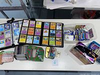 Wide shot of the lot showing binders with Pokémon trading cards, Minecraft playing cards tin, various loose cards and additional card tins arranged on a table.