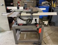 Front view of Ryobi BT 3000 table saw showing main body, base stand, sliding side table, adjustment handle, and power cord.