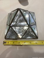 Glass pyramid prism showing faceted beveled glass panels and dark metal framing, with measuring tape for scale indicating approx. 4.5 inches at base.