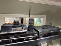 Photo showing all three devices on a shelf: Uniden scanner, Toshiba VHS/DVD combo player, Toshiba VCR with remote.