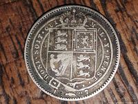 Reverse of the 1887 silver Victorian one shilling coin showing the crowned shield with quartered lions and unicorn with legend inscription.