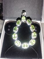 Pendant displayed in black jewelry box with velvet padding showing its pear-shaped arrangement of 10 green amethyst stones set in silver.