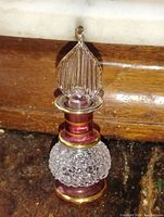 Perfume bottle upright showing cranberry colored glass with clear textured glass body and gold band trim with ribbed clear glass stopper.