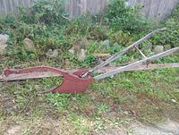 Full side view of antique iron horse-drawn plough showing wooden handles and rust-red painted metal blade and frame.