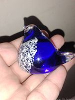 Photo of cobalt blue blown glass bird paperweight showing white speckled chest and polished smooth surface held in hand.