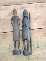 Pair of two African ebony carved statues standing on wooden pallets outdoors, showing full front view and details.