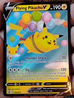 Close-up image of a Flying Pikachu V holographic Pokémon card with colorful balloons and attack details visible.